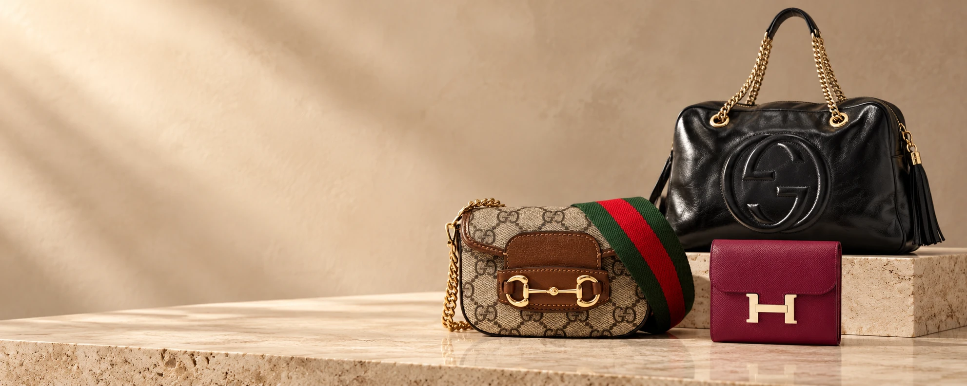 Editorial studio scene featuring luxury handbags and a burgundy wallet on warm stone
